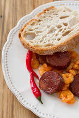 fried shrimps with sausages and red pepper on white plate on brown wooden background