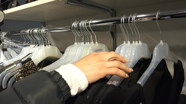 Woman&rsquo;s hands run across a rack of 