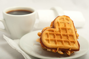 cup of morning coffee and fresh waffles in the shape of heart on