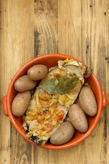 tuna with onion and potato in ceramic dish on brown wooden background