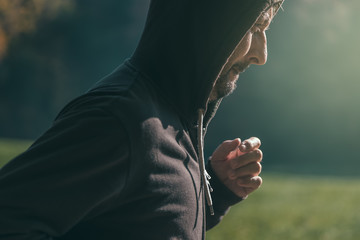 Hooded man jogging in the park in early autumn morning