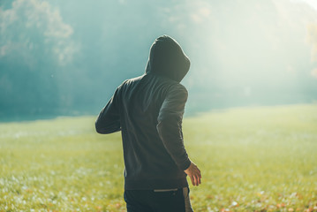 Hooded man jogging in the park in early autumn morning