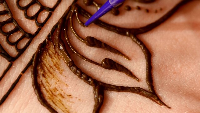 Process of decorating woman hand with henna tattoo, mehendi, on black, close up, cam moves top down