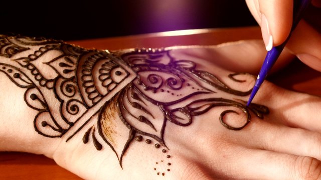 Womans hand being decorated with henna tattoo, mehendi, on black