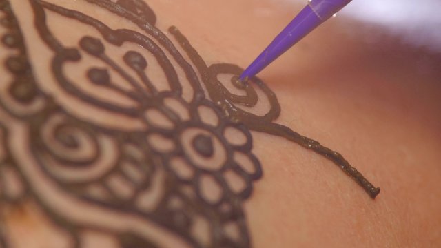 Process of decorating womans back with henna tattoo, mehendi, on black, dynamic change of focus