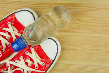 Fototapeta na wymiar Sporting red shoes on a wooden background with a bottle of water