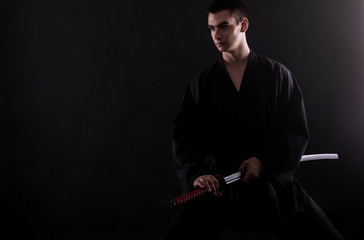 Young martial arts fighter with katana on black background