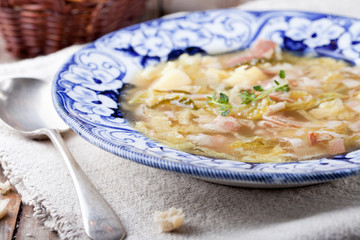 Cabbage soup with bacon, potato, meat, ceramic plate, bread 