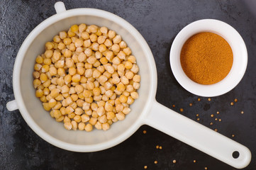 Boiled chickpeas in a colander and spices on black metal background