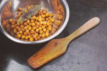 Chickpeas baked with spices in metal bowl and wooden spatula on black surface with place for text