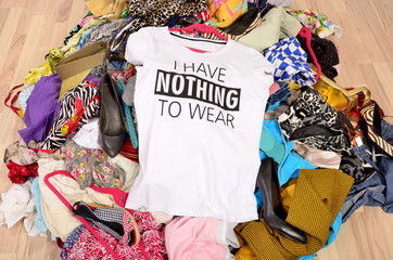 Big pile of clothes thrown on the ground with a t-shirt saying nothing to wear. Close up on a untidy cluttered wardrobe with colorful clothes and accessories, many clothes and nothing to wear.