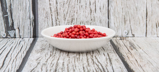 Pink peppercorn in a white bowl over wooden background