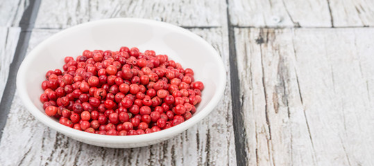Pink peppercorn in a white bowl over wooden background