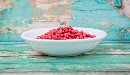 Pink peppercorn in a white bowl over wooden background