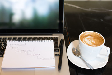 Workplace, laptop and notepad with hand drawn business plan sele