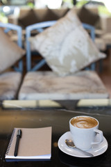 Hot latte art coffee cup on wooden table and note book.