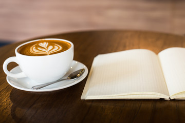 Hot latte art coffee cup on wooden table and note book, vintage