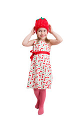 A joyful little girl in a knitted beanie cap in the form of strawberries