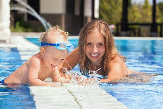 Laughing little baby boy in underwater goggles with happy mother having fun in pool before swimming lesson. Healthy lifestyle, water sport activity with active parents on family vacation with child.