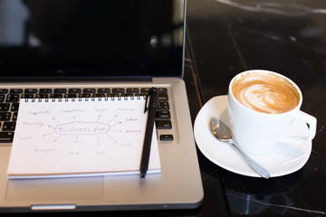 Workplace, laptop and notepad with hand drawn business plan sele