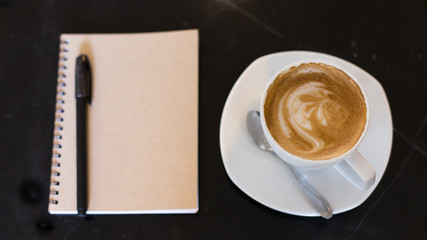 Hot latte art coffee cup on wooden table and note book.