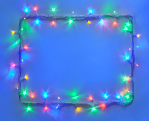 Christmas lights frame on blue background with copy space.