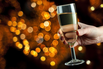 a glass of champagne in the hand of the woman on a background of twinkling lights garlands