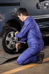 Fototapeta na wymiar Male Mechanic Fixing Car Tire At Repair Shop