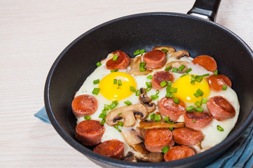 fried eggs with mushrooms and sausage in a frying pan