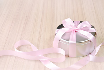 Gift in round tin box with pink ribbon background
