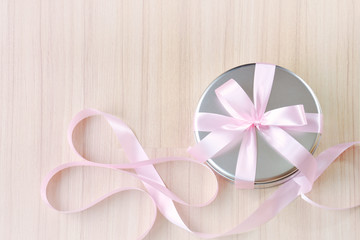 Gift in round tin box with pink ribbon background (top view)
