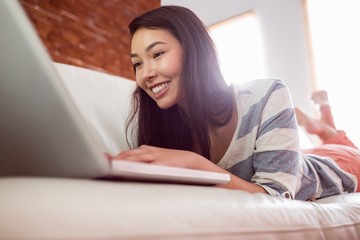 Smiling asian woman on couch using laptop