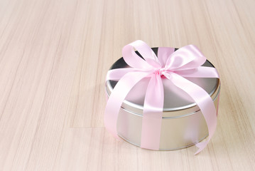 Gift in round tin box with pink ribbon background
