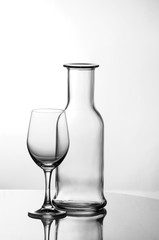Empty wine glass next to an empty glass bottle - both are completely transparent.
