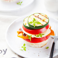 Grilled vegetables, cheese gratin stacked on a plate, fresh basil .