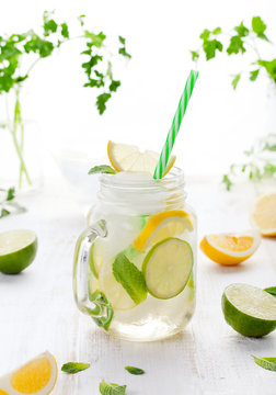Lemonade with ice, lemon and lime slices in jar, straw.