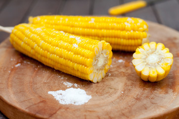 Boiled sweet corn cobs with salt on  wooden background