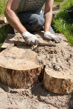 Worker making a walk path in garden decorated with wooden stumps