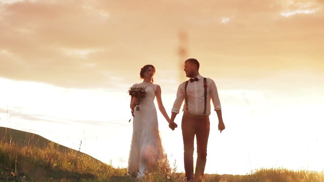 bride and groom holding hands walking in the sunset