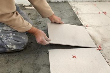 Home renovation, worker placing tiles to mix of sand and cement