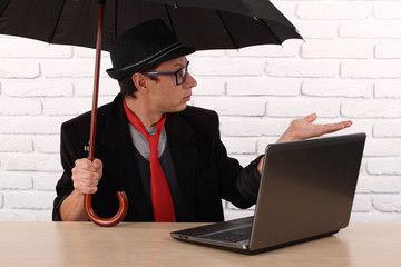 man sitting at the table with laptop and holding umbrella