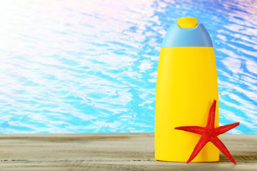 Bottle of suntan cream with sea star on table on water background