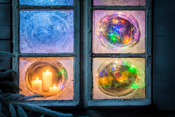 Beautiful burning candles for Christmas in frozen window at eve