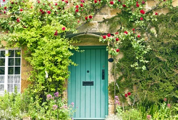 Wall murals Old door Green wooden doors in an old traditional English stone cottage surrounded by climbing red roses and flowers