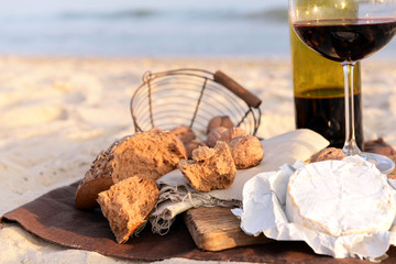 Beautiful romantic composition of red wine, bread and nuts on sandy beach, close up