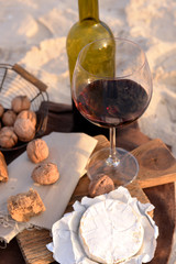 Beautiful romantic composition of red wine, bread and nuts on sandy beach, close up