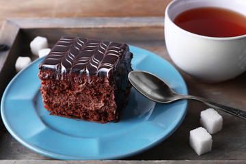 Sweet chocolate cake on blue plate with cup of tea on wooden tray