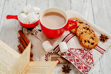 
winter mood , cocoa with marshmallows in a red cup , cinnamon and cookies with chocolate on a...
