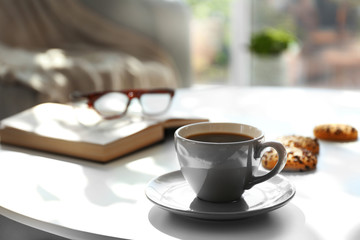 Cup of coffee with biscuits on table in room