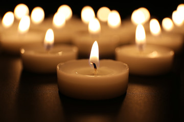Alight candles in a row on black background, blurred
